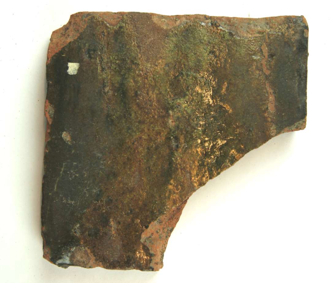 1 fragmenteret gulvflise af rødbrændt lergods med grønligstribet blyglasur på oversiden. Sidemål ca. 13 cm. tykkelse ca. 2,1 cm. 