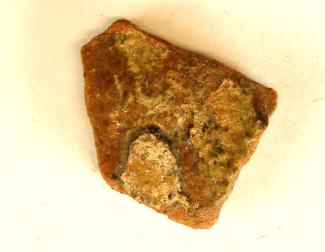 1 sideskår af rødbrændt lergods med bladskæl af pibeler på ydersiden, der er dækket af klar til grønlig blyglasur, gruppe 1.