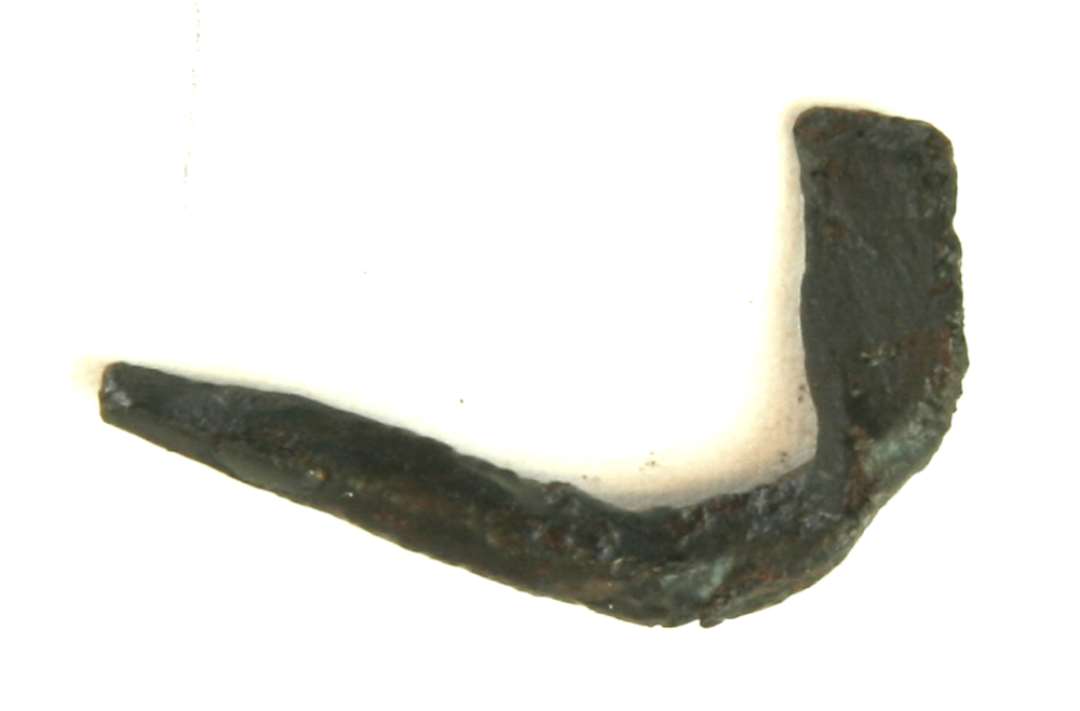 1 forvredet, ombøjet jernstump af flad form i den ene ende. Længde 2,7 cm. Bredde 1,9 cm.