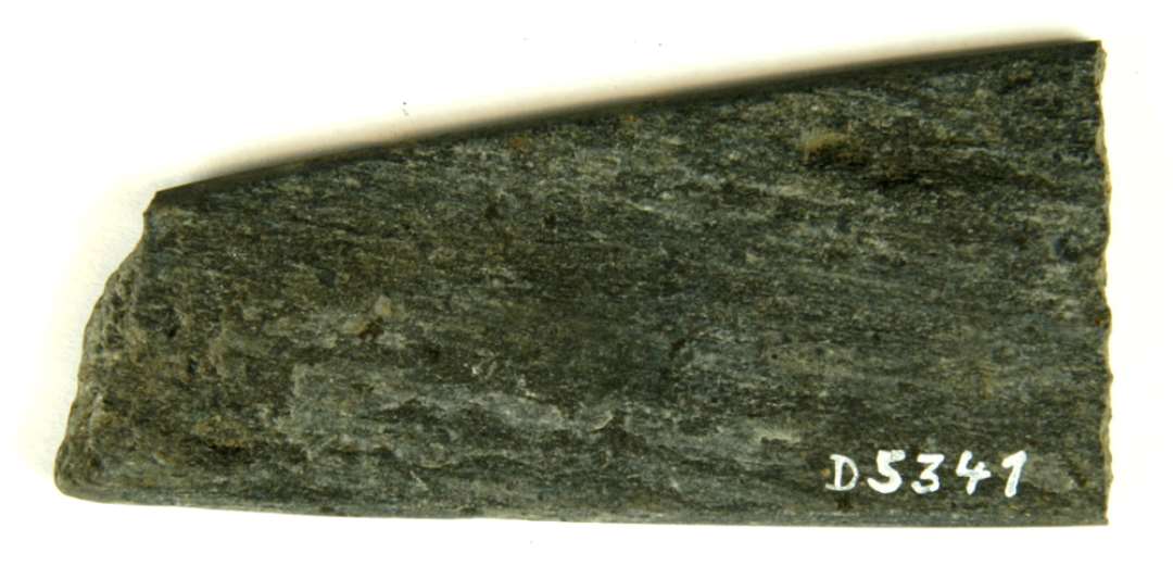 1 fragment af pladeformet hvæssesten af grålig skifer. Stykket har afrundede kanter og jævn tilspidsning mod den ene ende. L : 7,9 cm. St.br : 3,6 cm. Tyk : 0,6 cm.