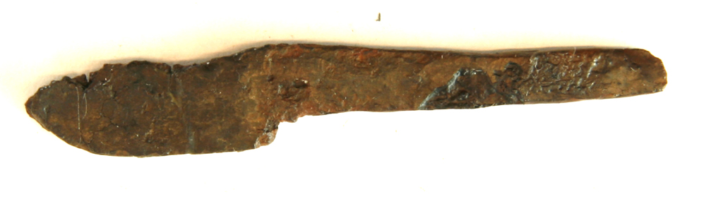 1 miniaturekniv af jern med flad forsænket skafttunge og bladryg med nedadkrummet spids. L : 6,6 cm. Heraf skafttunge : 4 cm.