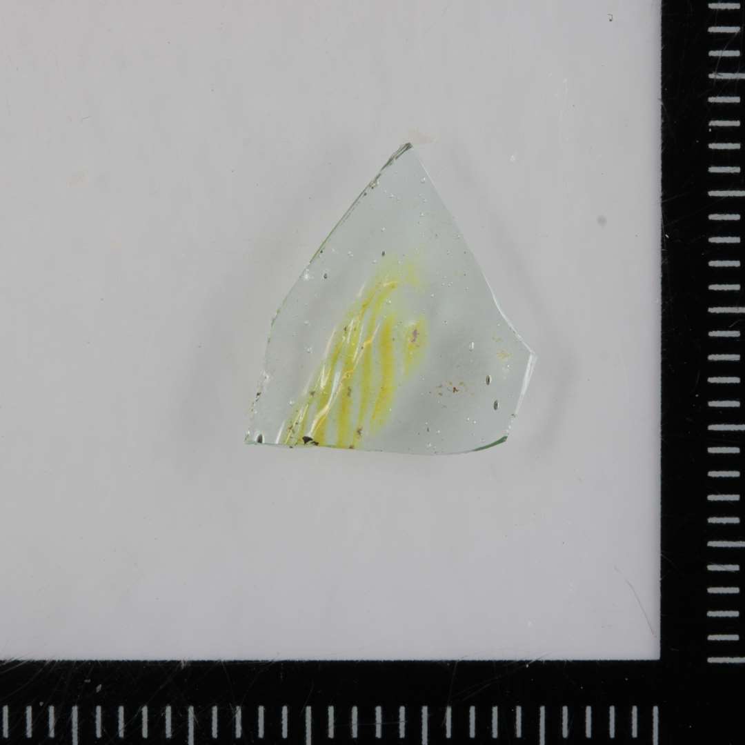 1 sideskår af gennemsigtigt, svagt grønligt glas med ismeltet fladt bånd af snoede gule glastråde. Reticella.