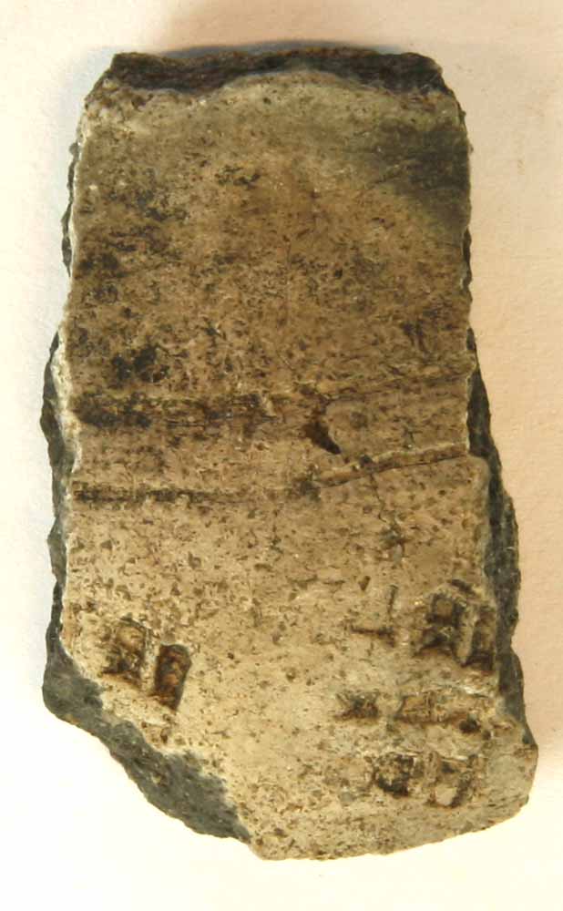 1 hals/skulderskår af gråbrunligt, magret lergods fra kar med udadbøjet rand. På skulderen ses vandrette furer og indstemplet ornamentik, gruppe 5.