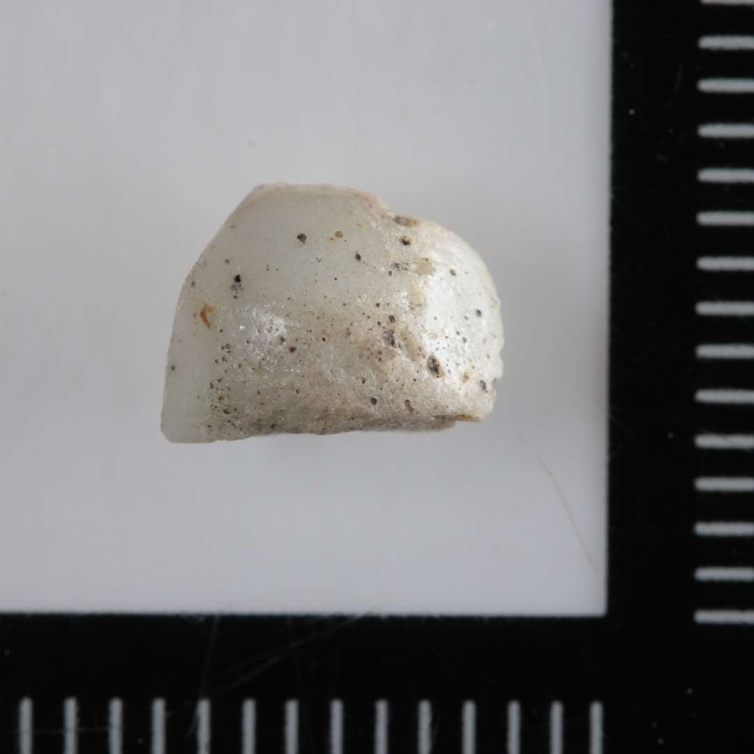 1 ubetydeligt fragment af tøndeformet perle af uigennemsigtig hvidgrå glasmasse.
