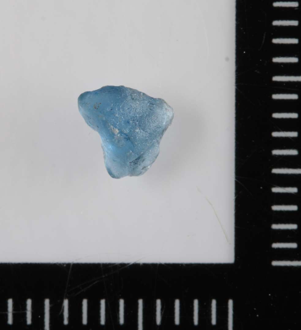 1 ubetydeligt fragment af gennemsigtigt, blåligt, smeltet glas.