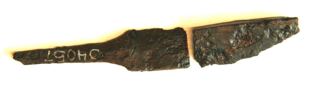 1 forrustet fragmenteret jernkniv (betegnet DD) med smal skafttunge. Totallængde: 10 cm. heraf skafttunge 3,3 cm. bredde 1,2 cm. 