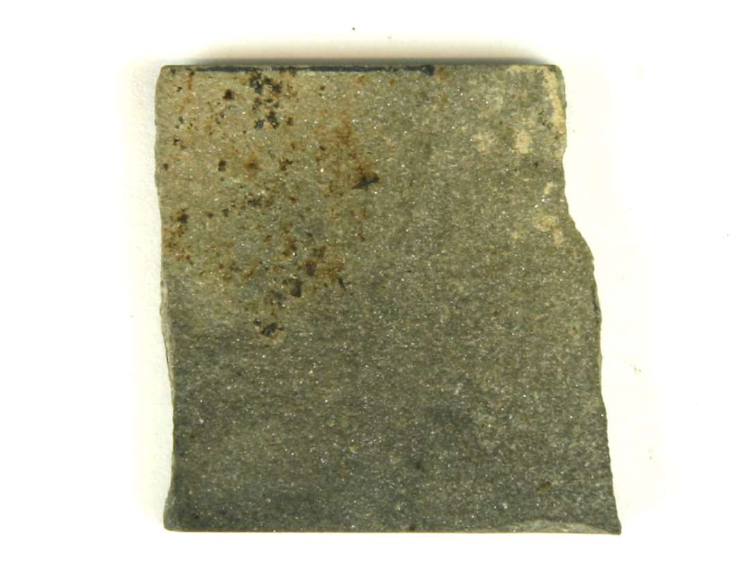 1 stk. næsten kvadratisk, tyndt stk. sandsten. 2 af smalsiderne synes oprindelig at have været del af en større tildannet flade. Største mål: 3,4x3,6 cm.