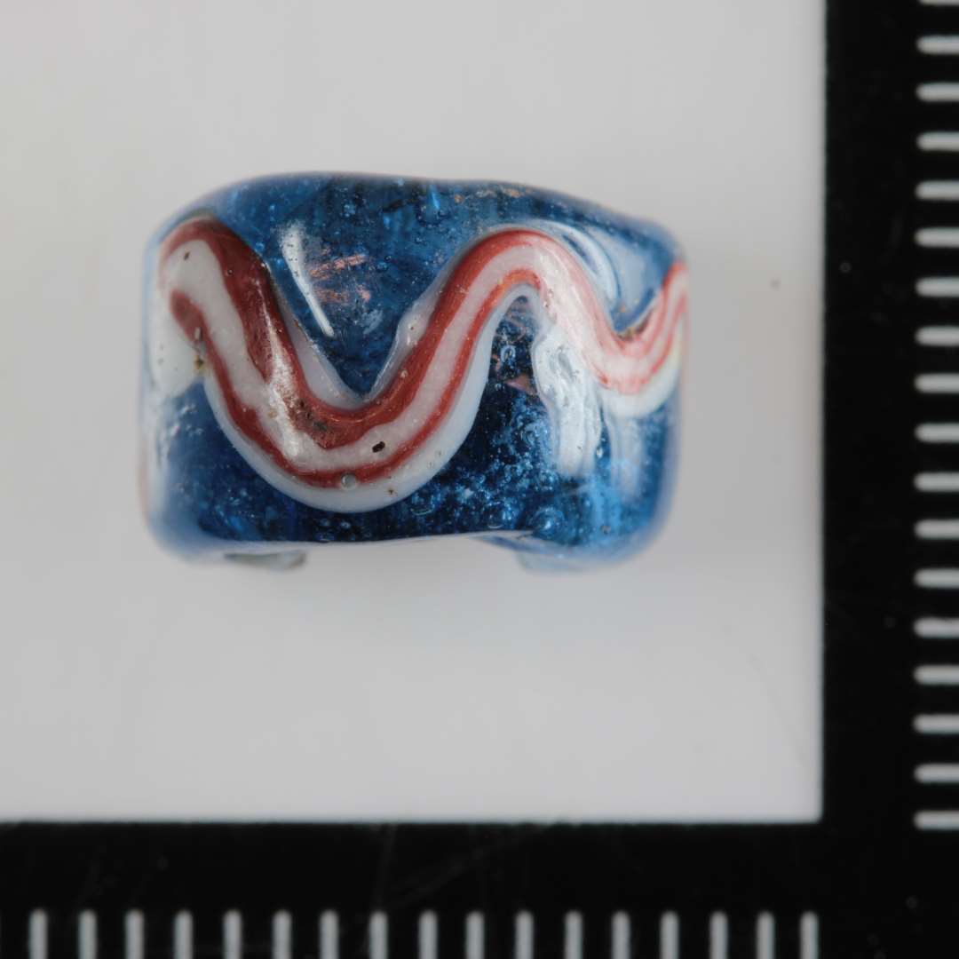 1/2 perle af bred ringform af gennemsigtig blåt glas med påsmeltet bølgelinie af uigennemsigtig rød- hvidstribet glasmasse på ydersiden.