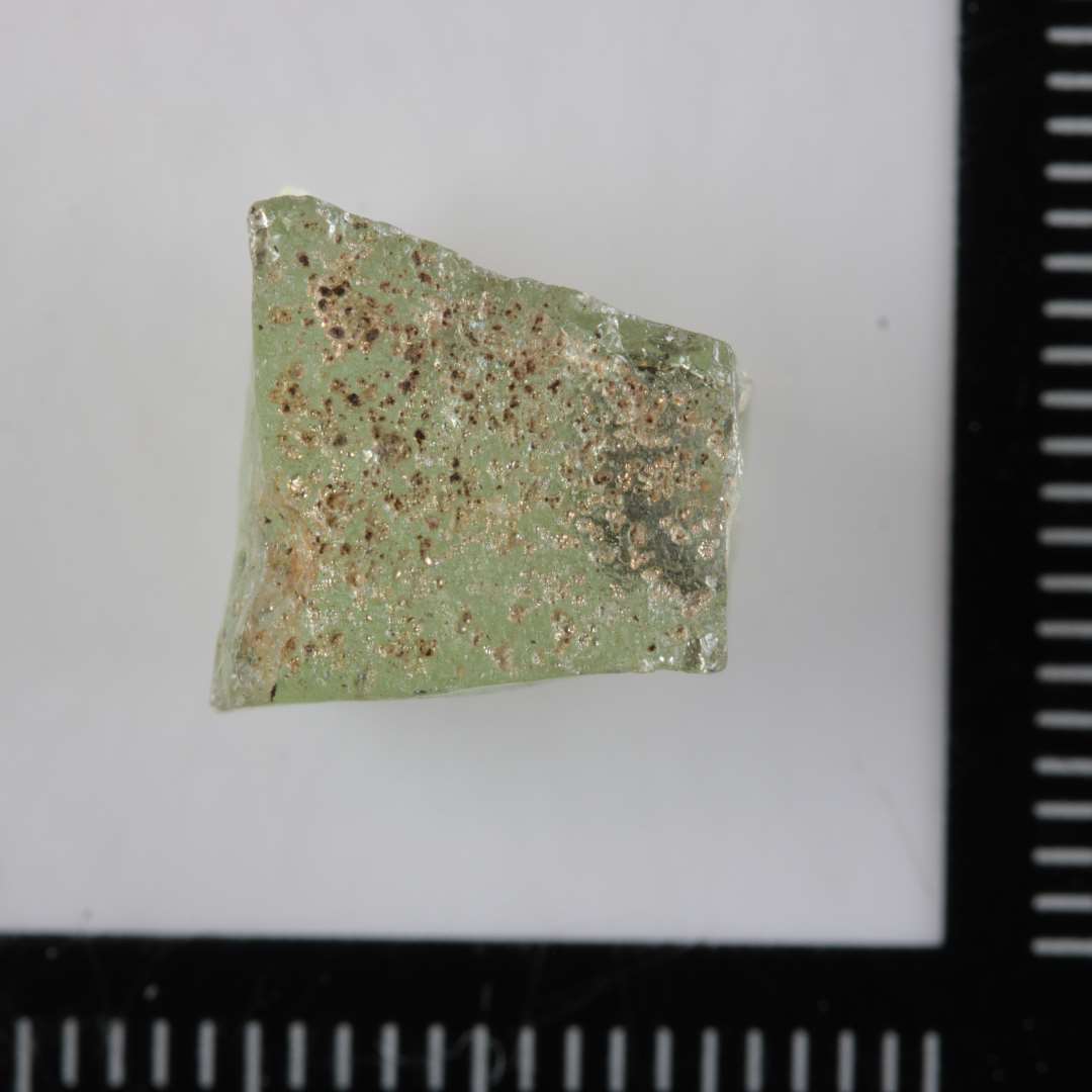 1 mosaikstift af gennemsigtig svagt grønlig glasmasse med spor af guldfoliebelægning på den ene sideflade.