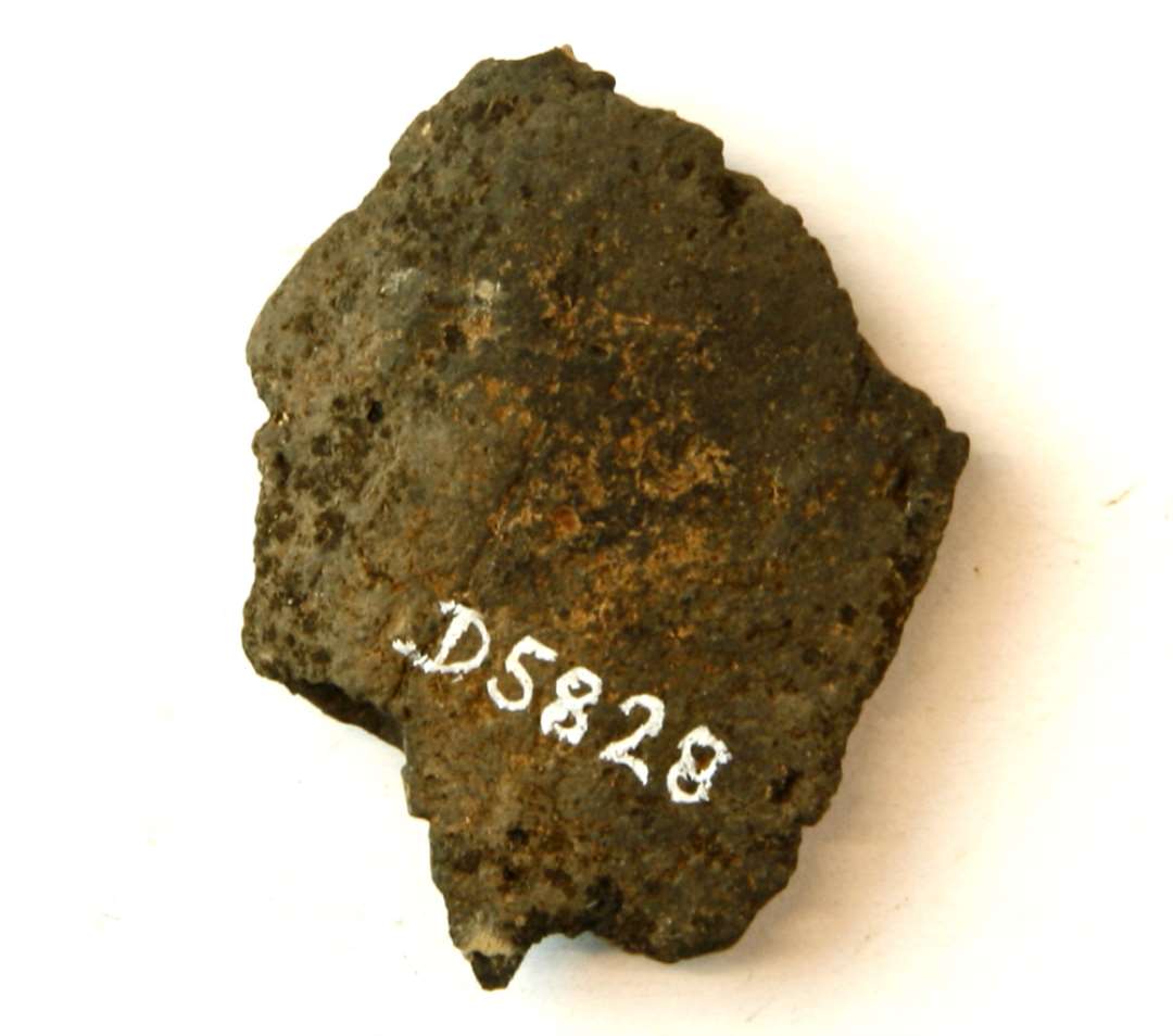 1 afsprængt flad stump antagelig af discosformet vævevægt af gråbrændt lermasse. Største mål:  4,5 cm.