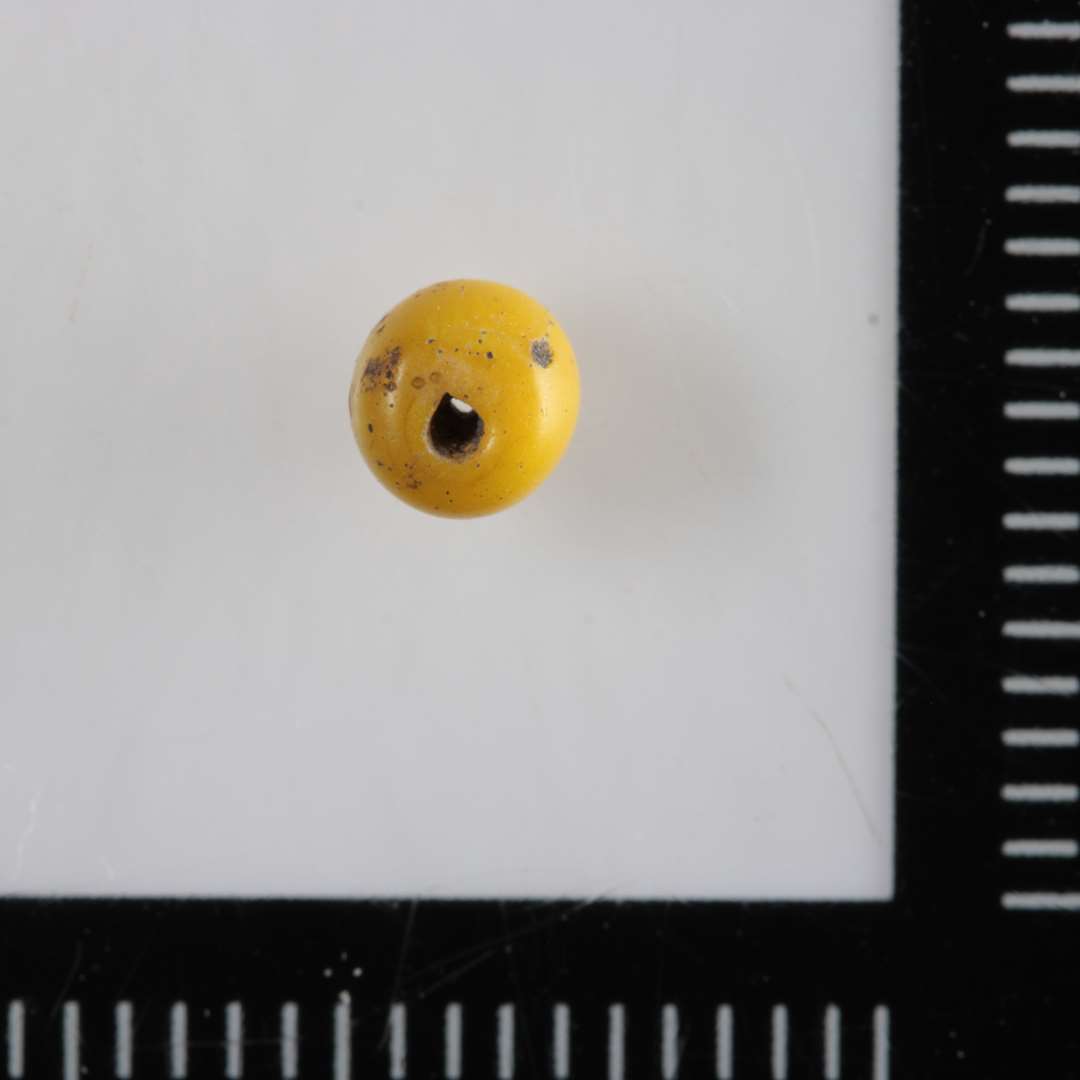 1 ganske lille, uigennemsigtig gul glasperle af kugleform.
