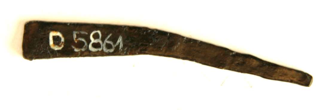 1 stk. let krummet jern af flad tilspidset form. L : 5,3 cm. Knivbladsskafttunge? 