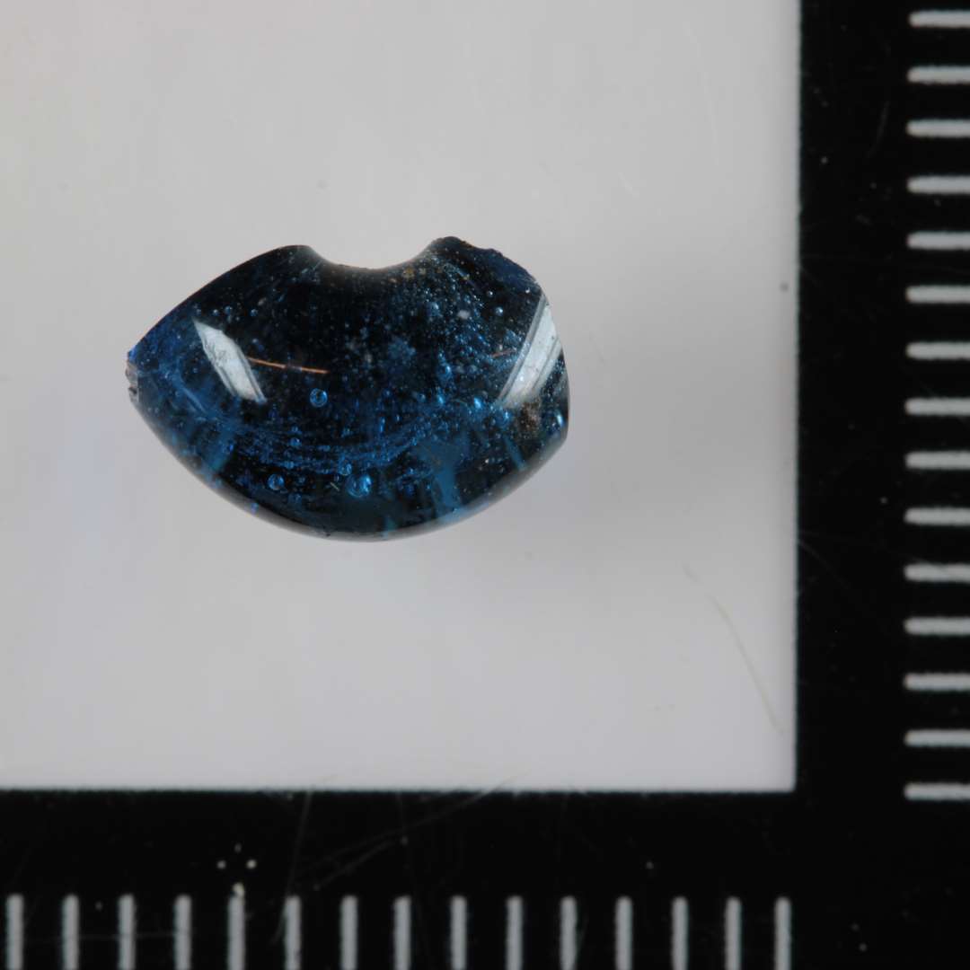 1 perle af klart, blåt glas, ca. halvdelen bevaret.