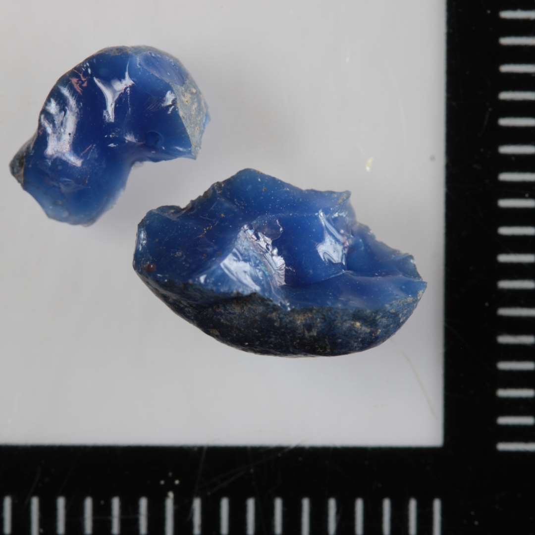 1 fragment af smeltet glasklump af fladtrykt kugleform og af uigennemsigtig blå masse.