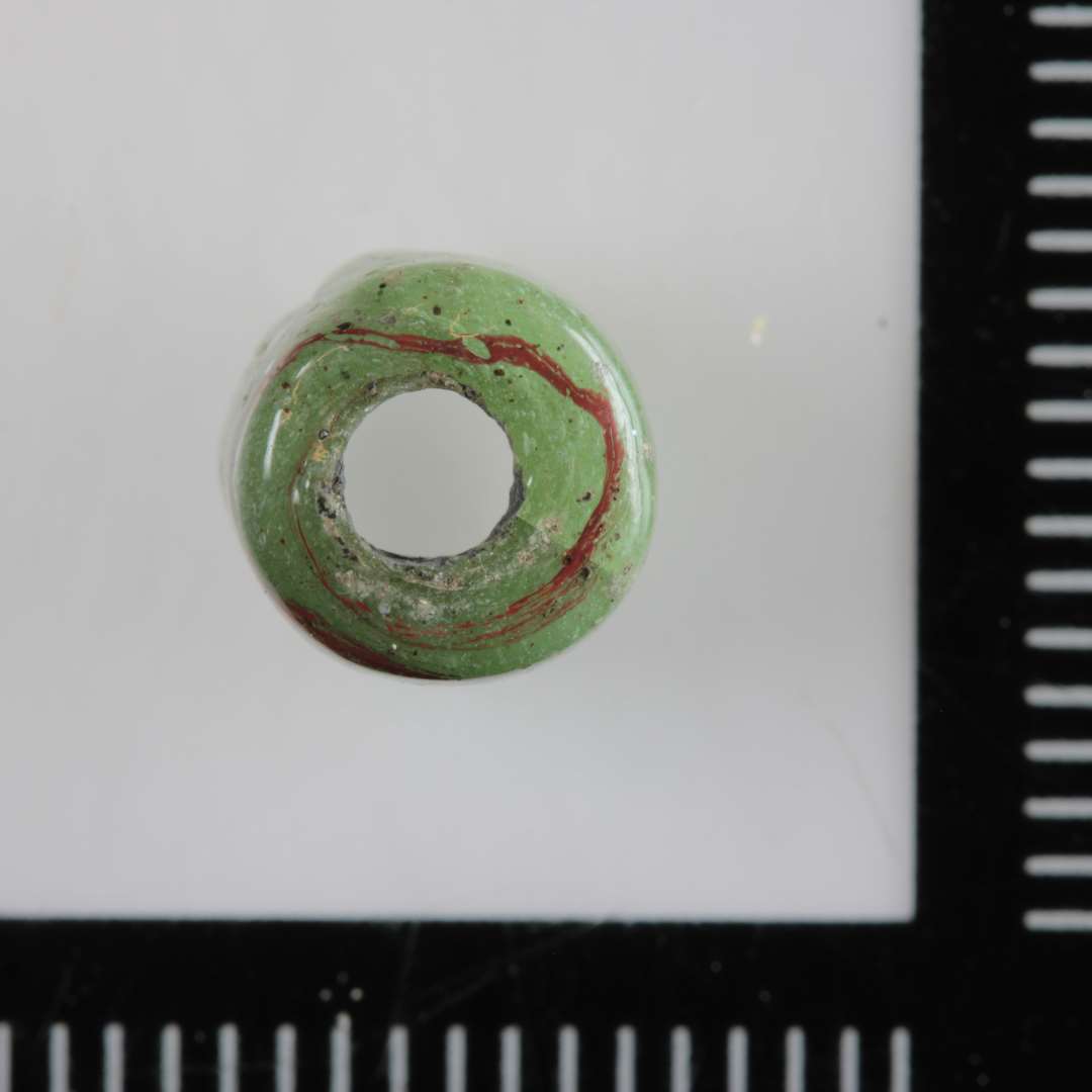 1 cylinderformet perle af uigennemsigtigt lyst grønligt glas med rødt strejf. 8 mm.