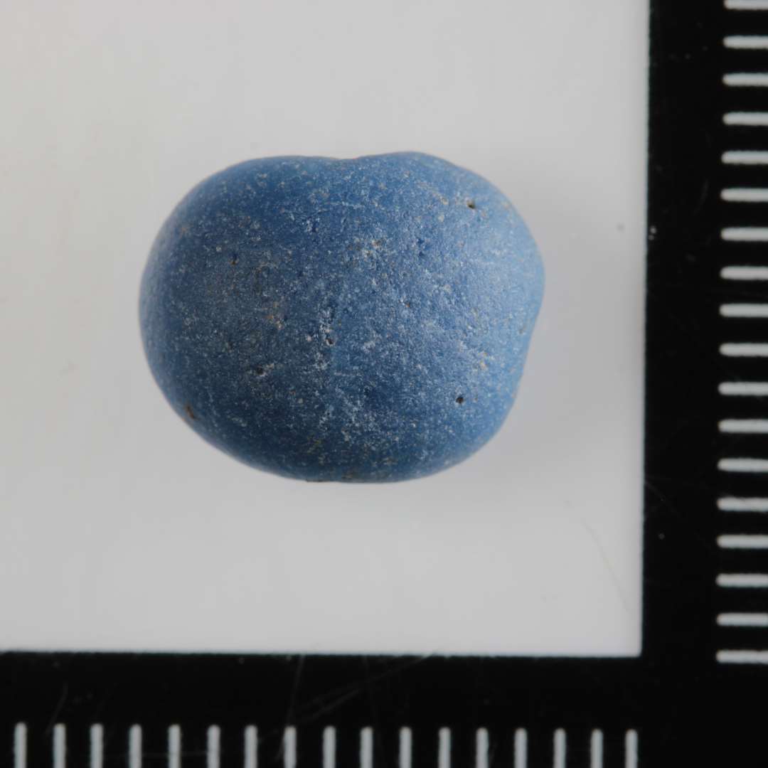1 fragment af perle af klart, blåt glas. Vanderoderet.