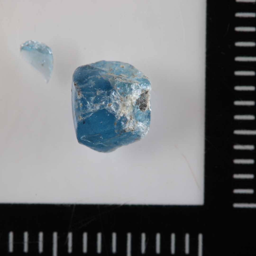 1 ubetydeligt fragment af perle af fladtrykt kugleform af delvis gennemsigtigt  blåligt glas.