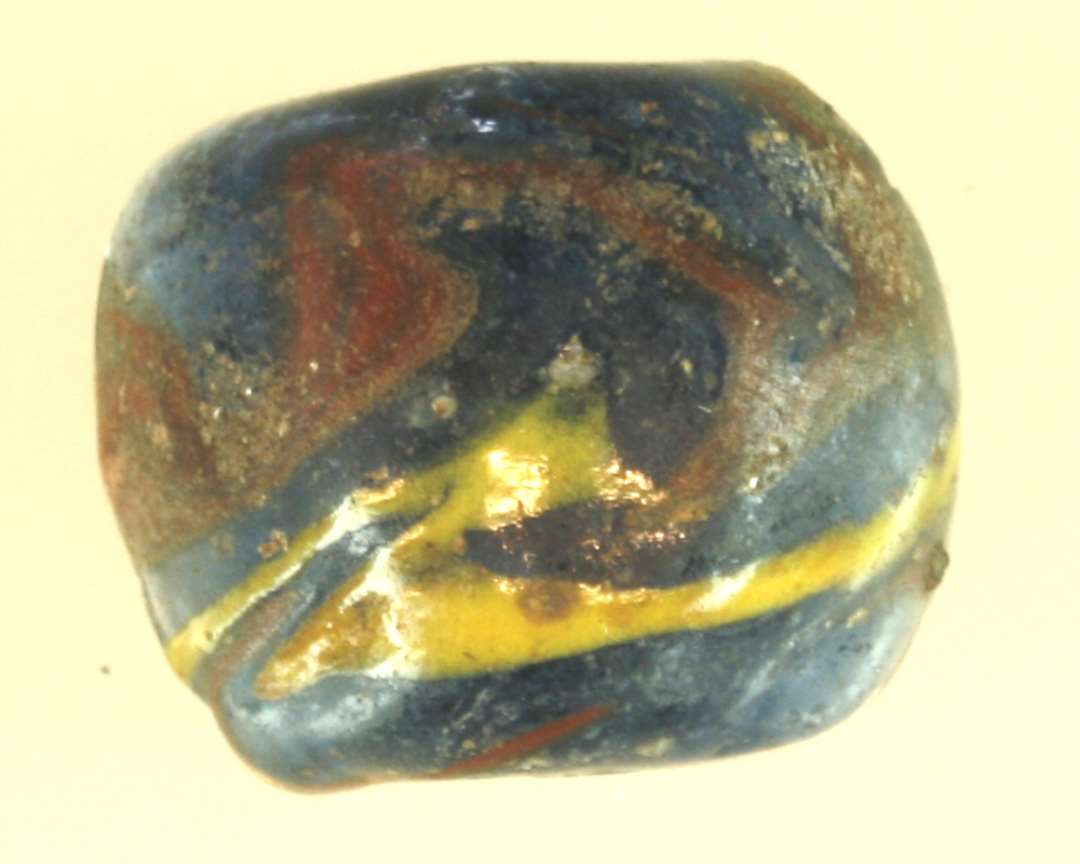 1 perle af blåt glas med pålagt slyng af gult og rødt glas. Halvdelen bevaret.