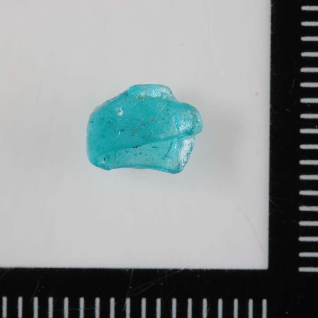 1 fragment af perle ( mislykket forarbejde ? ) af gennemsigtigt, blåligt glas.