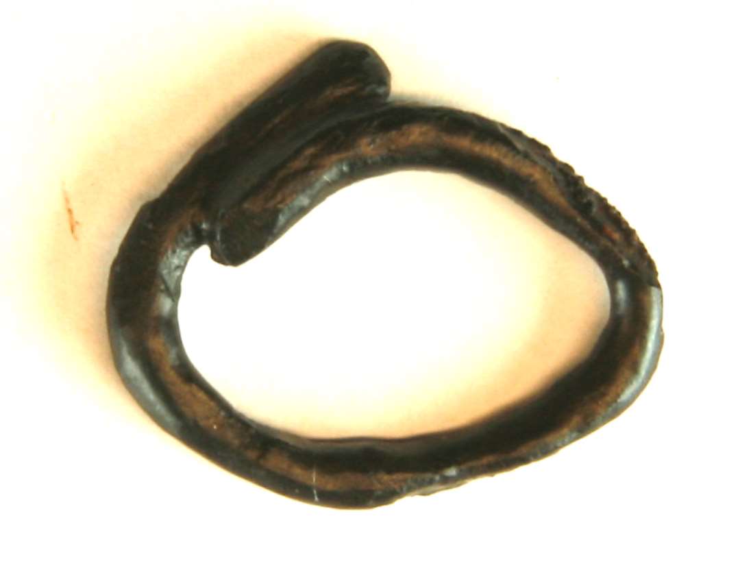 1 forrustet jernring af fortykket oval form med opbrudt sammenføjning. Ringen har uregelmæssig oval tværsnitsform, ca. 0,25 x 0,3 cm. Ydre mål 2,1 x 2,5 cm.