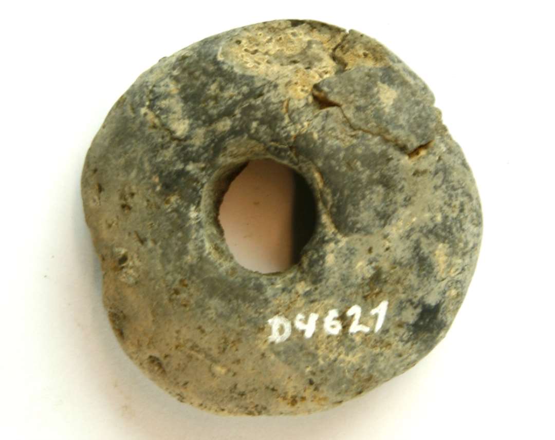 1 fragmenteret af discosformet vævevægt af gråbrunligt lermasse. Diameter ca. 6,1 cm.