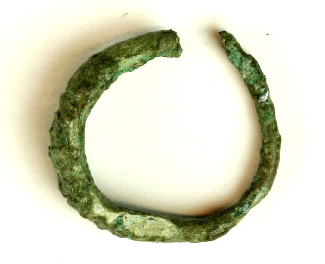 1 mandsfingerring af bronze med fortykket vertikalt rillet overside. Ringen er sprunget op i sammenføjningen i den ene side. Største diameter 2,6 cm.