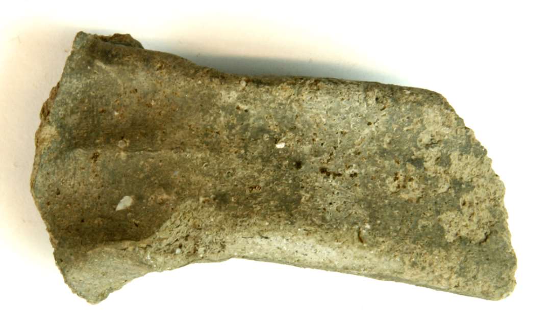 1 fragmenteret kandehank af gråbrændt magret lergods. Hanken har rektangulær tværsnitsform med afrundede hjørner og bred, flad fure på oversiden, gruppe 0.