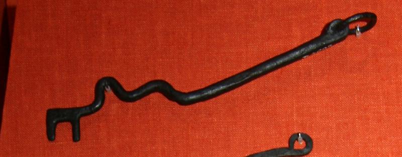 1 jernnøgle tildannet af en trind jernstang, hvis ene ende er ombøjet til et øje der omslutter en omtrent cirkulær jernring knap 2 cm i diamenter, medens den modsatte ende afsluttes med en simpel togrenet kam bag hvilken nøglestangen bøjer sig op i to slangerygskrumninger. Længde med ring ca. 16 cm.