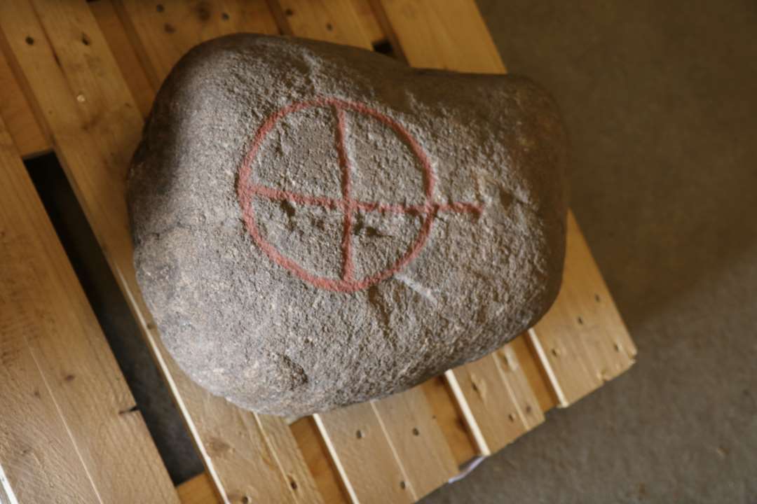 Hjulkorssten. Klumpet sten i brun granit. Midt gennem hjulet en hugget rende til flækning af stenen. 0,52 m. x 0,39 x 0,24 m.