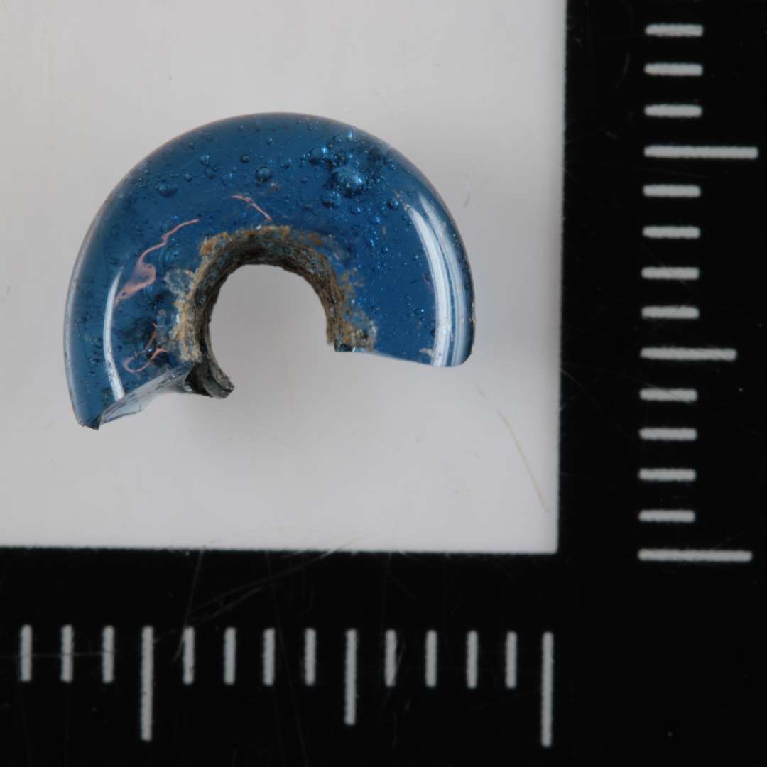 1/2 perle af afrundet ringform og af gennemsigtigt blåligt glas. 