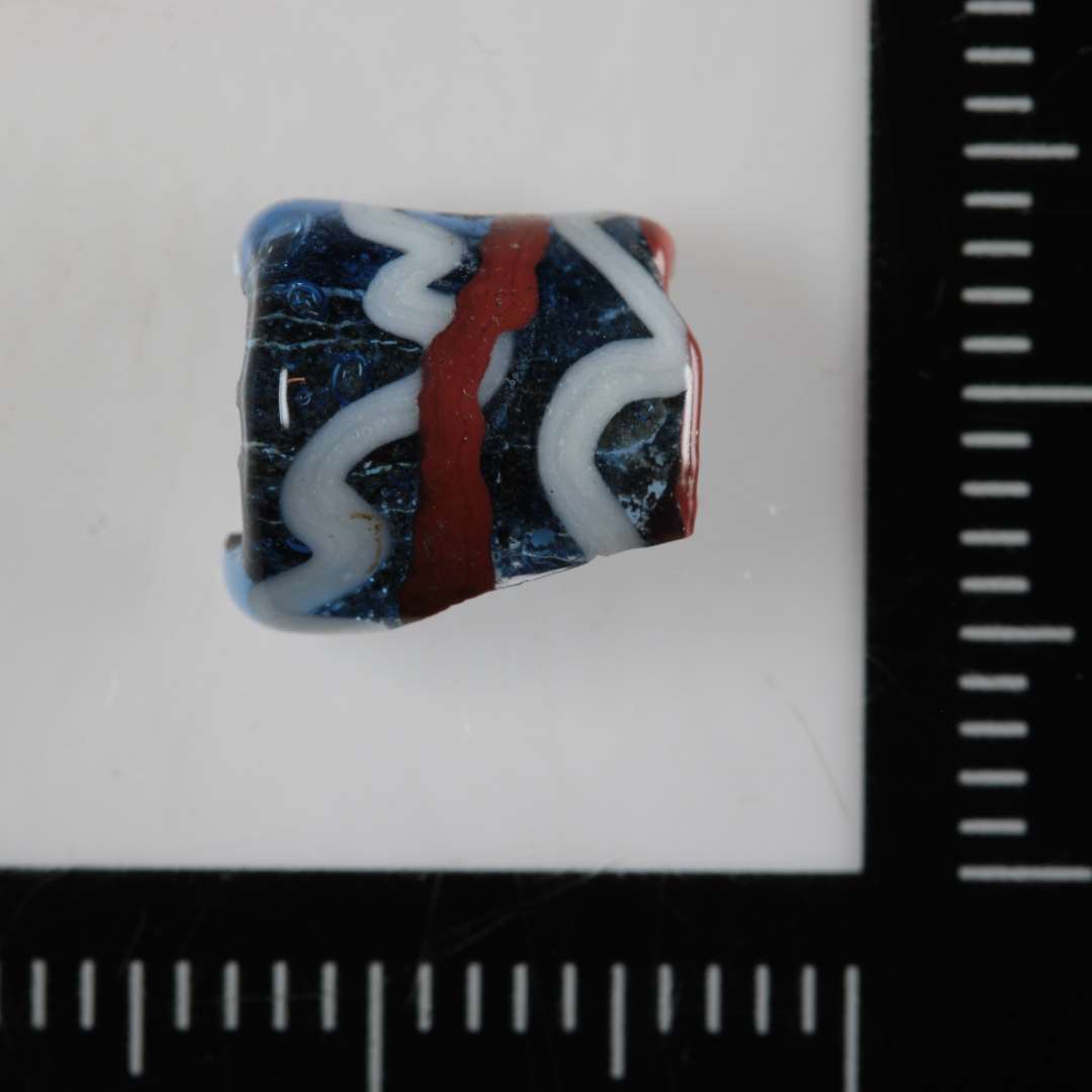 1/2 cylinderformet perle af blåligt gennemsigtigt glas med indsmeltede streger i rød og bølgelinier i hvid, uigennemsigtig glasmasse på ydersiden. 