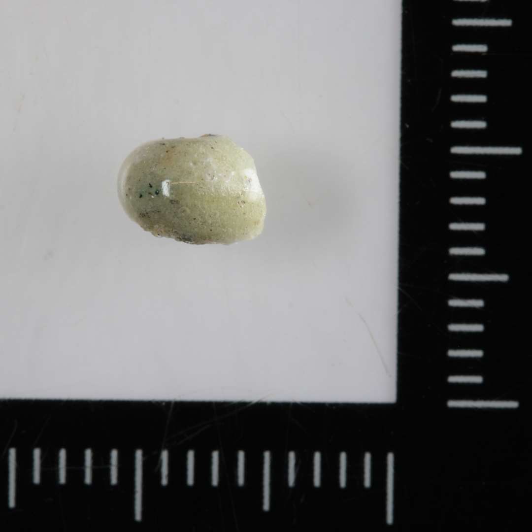 Fragment af ½ perle af uigennemsigtig grålig glasmasse.
