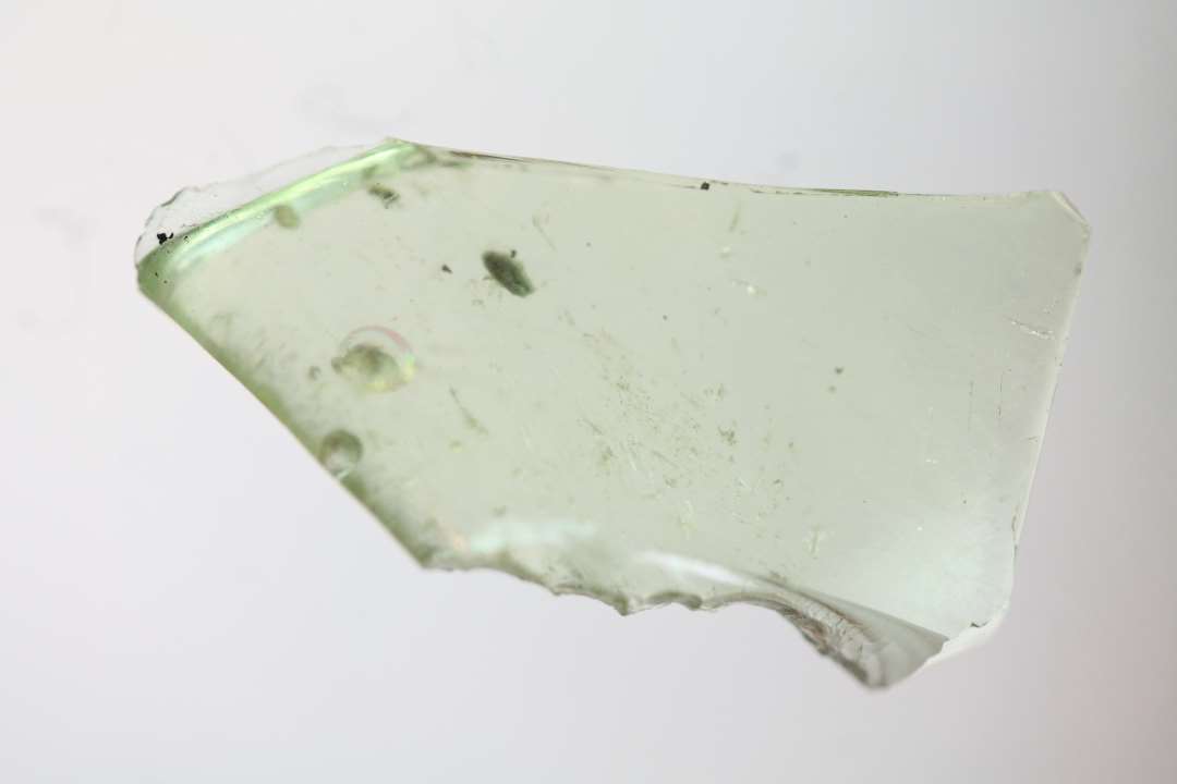 1 randskår med glat afrundet randkant fra bæger af klart grønligt glas hvori enkelte luftblærer. St. mål: 1,5 x 1,8 cm. godstykkelse: 0,2 cm.
