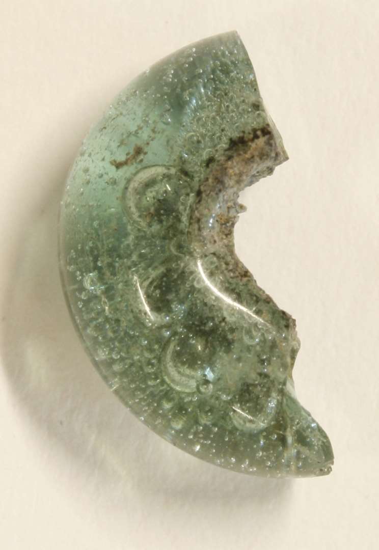½ ringformet perle af klart grønblåligt glas hvori talrige større og ganske fine luftblærer. Bredde (diam.) 1,25 cm. Tykkelse: 0,5 cm.