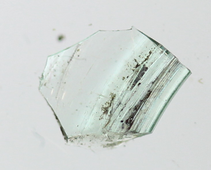 1 glasskår af tyndvægget, let grønligt gennemsigtigt glas af svagt buet/bølget form. St. mål: ca. 1,0 x 2,1 cm.