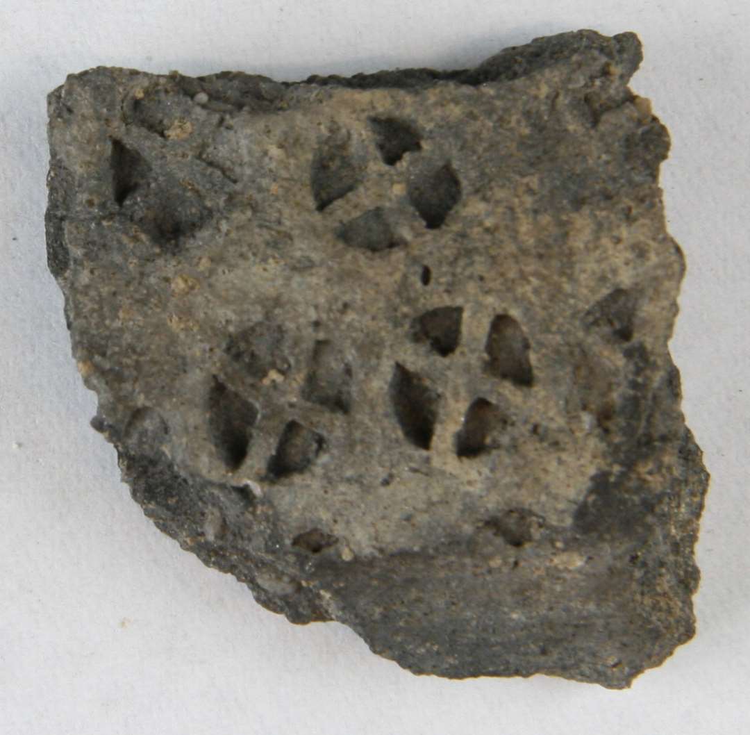 1 skulderskår af gråbrændt, magret lergods med tæt anbragte indstemplede hjulkorsornamenter. Det enkelte ornament er 0,7 - 0,8 cm. i diameter.