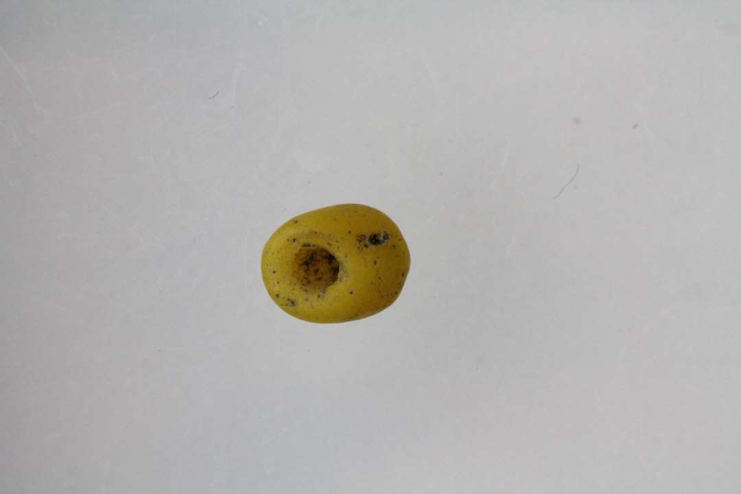 1 skråt afbrudt ende af cylinderformet perle af gult ugennemsigtigt glas. Diameter: 0,4 cm.