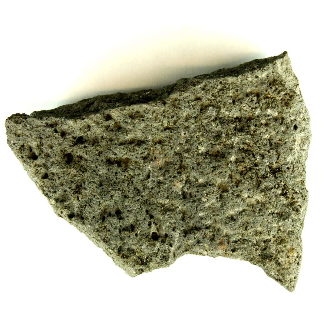 Fragment af kværnsten af grålig basalt. Et stykke af stenens cirkulære yderkant er bevaret, medens de øvrige kanter fremtræder som brud. Stenens ene side er grubehugget: plan men med ret talrige smågruber. Den modsatte side udviser en ujævn afsprængt overflade. Største længde: ca.17,7 cm. Bredde: ca. 14 cm. Største tykkelse: 6,5 cm.