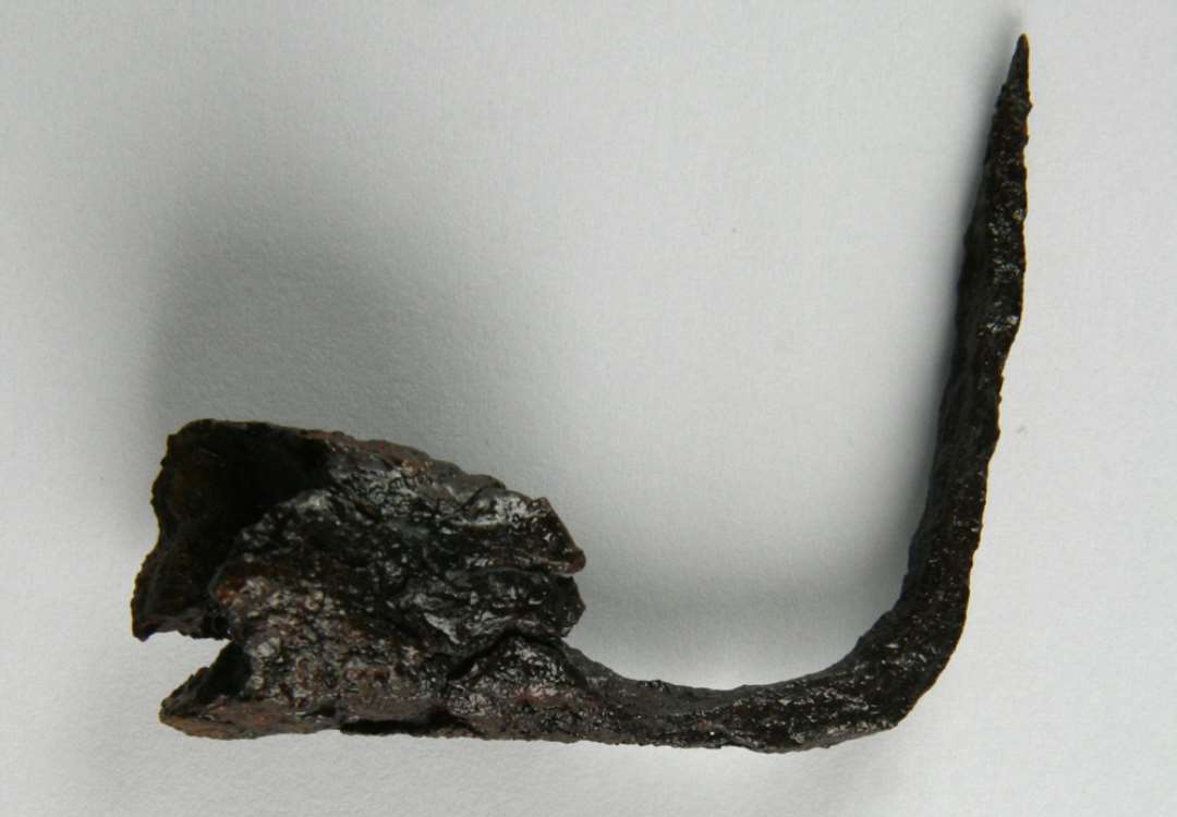 1 fragmenteret lysepibe af jern tildannet som et kræmmerhusformet pibehoved med åben bund anbragt for enden af den vinkelret ombøjdede stilk, hvis yderste spids er afbrudt. Hovedets diameter. ca. 1,8 - 1,9 cm. Lysepibens højde: 5,2 cm. Største bevarede længde: ca. 5,4 cm.
