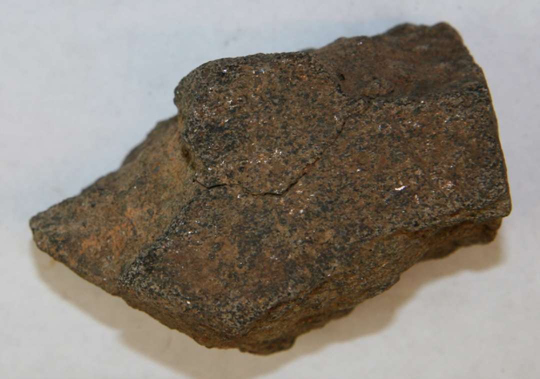 Avlssten af Glimmerskifer'.  Ildsprængt men tydeligt tildannet sten, ret forvitret på den ene side. Antagelig en avlsten. Mål: 7,3x4,3 cm.