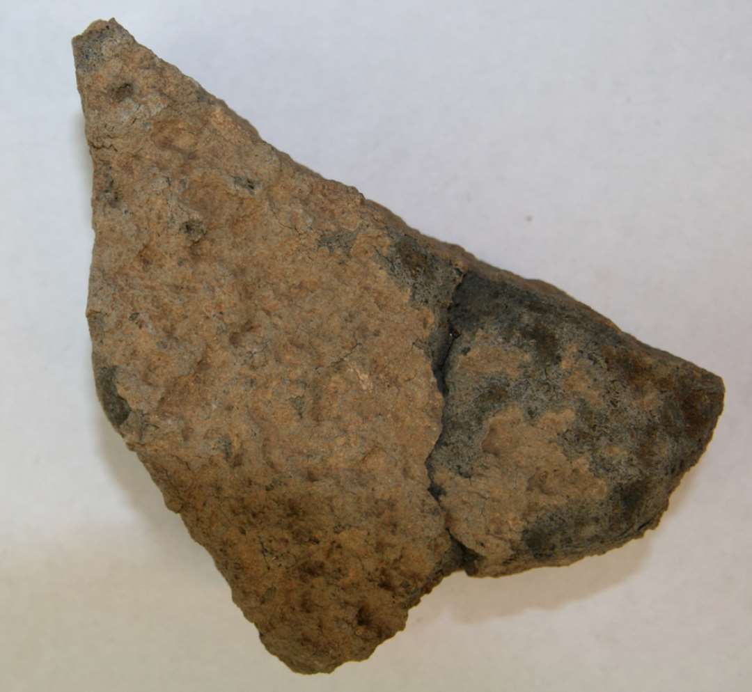 To sammenhørende, sammenlimede fragmenter af kværnsten af basalt. Ca. 4,8-6,0 cm tyk. Meget ujævn 'grube'-hugget underside.