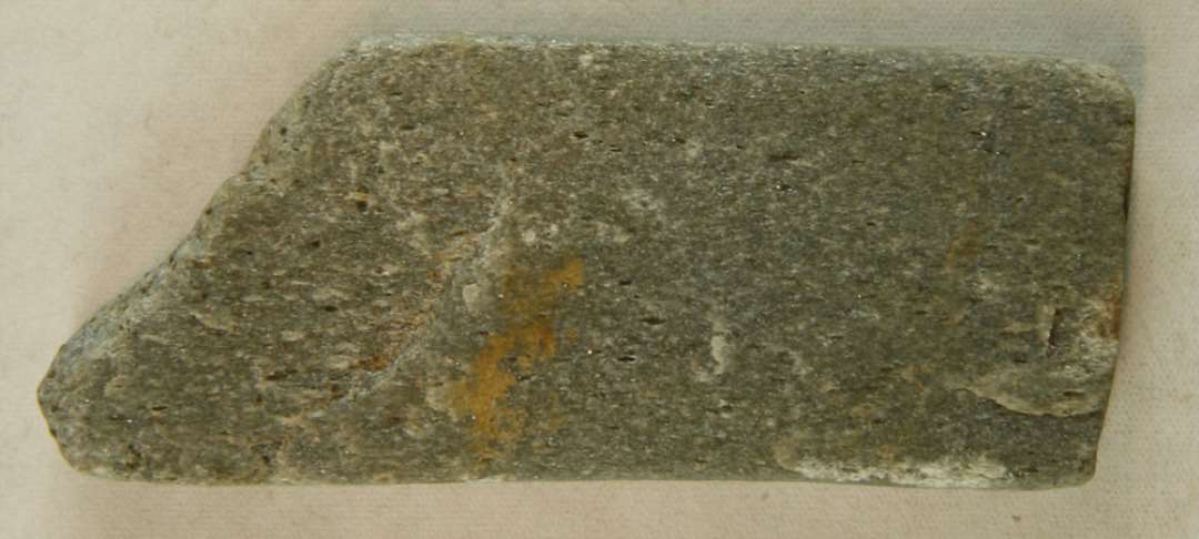Fragment af hvæssesten af Eidsborg skifer. Afbrudt i længden. Mål: 6,7x2,7x0,9 cm.