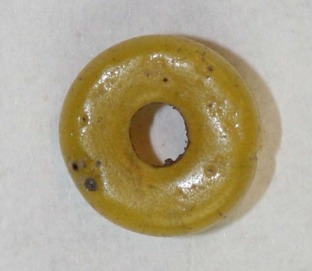 Ringformet, afskåret, hel, uigennemsigtig gul perle. Diameter: 0,7 cm.