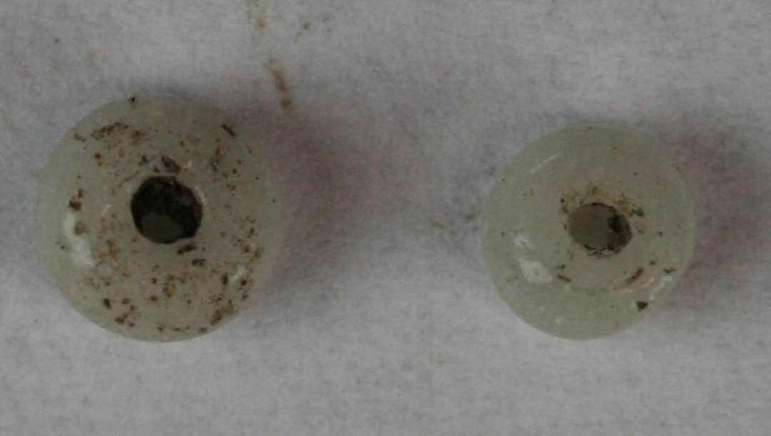 To ringformede, hele, afskårne, uigennemsigtige, hvidgrå perler. Diameter: 3 og 4 mm.