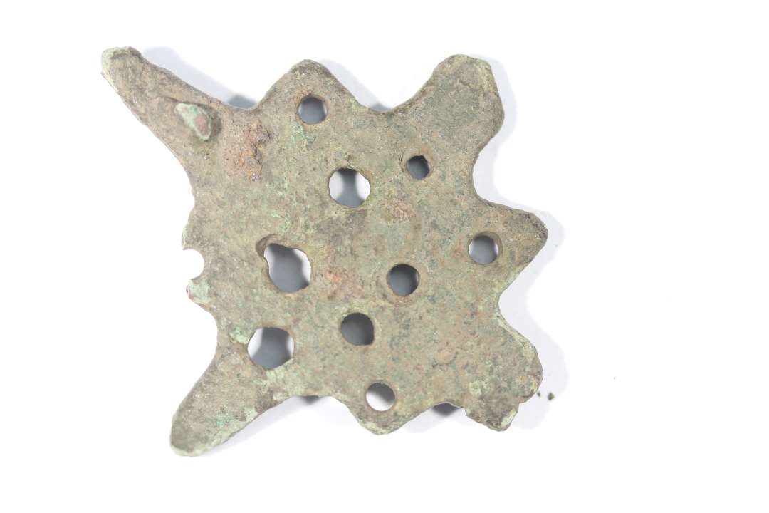 Fibula i bronze med langt udtrukne spidser, hvoraf de to kun er delvist bevaret. Lille krog til nålen på bagsiden. Største mål: 5x4,5 cm.