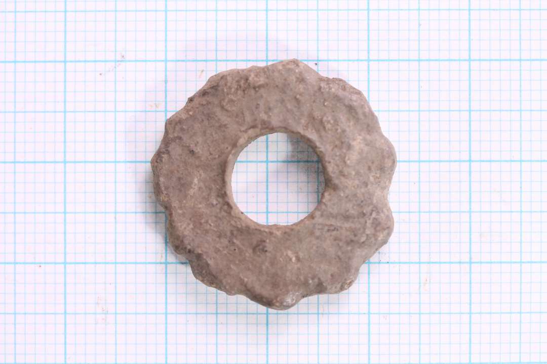 Flad, skiveformet stykke bly. diameter: 2,4 cm. Kanterne meget sjusket udført eller bølgende. Næppe vægt nok i den til at være tenvægt?
