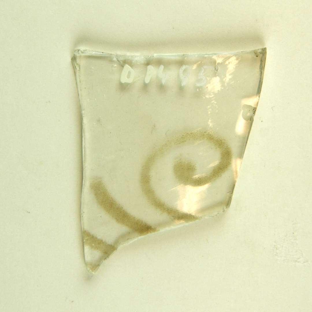 Fragment af glasrude af hvidt glas med rester af indslebet dekoration. Mål: 6 x 4,6 cm.