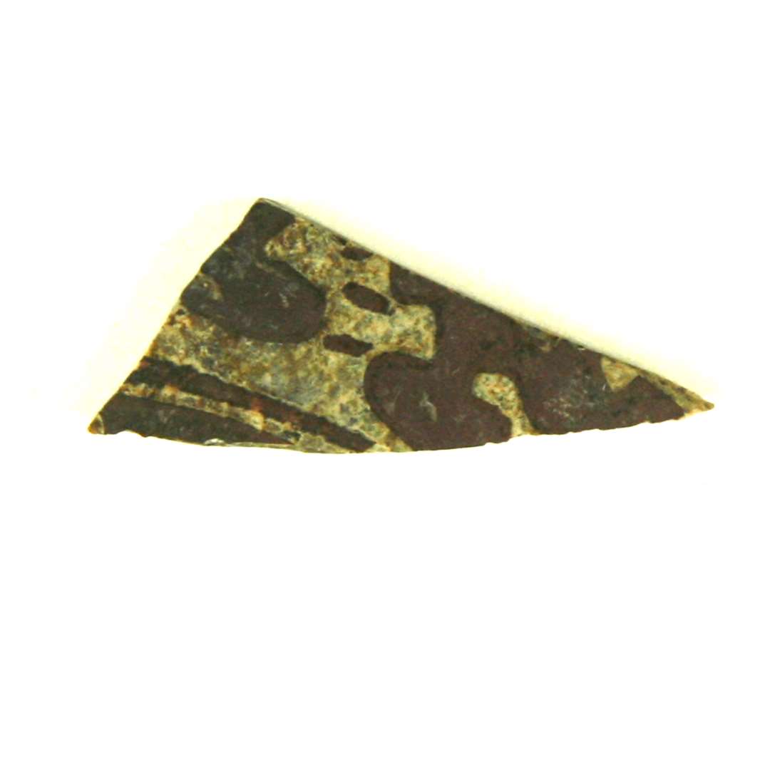 Fragment af rude af grønligt glas med rødbrun bemaling. Mål: 2,7 x 1,0 cm.