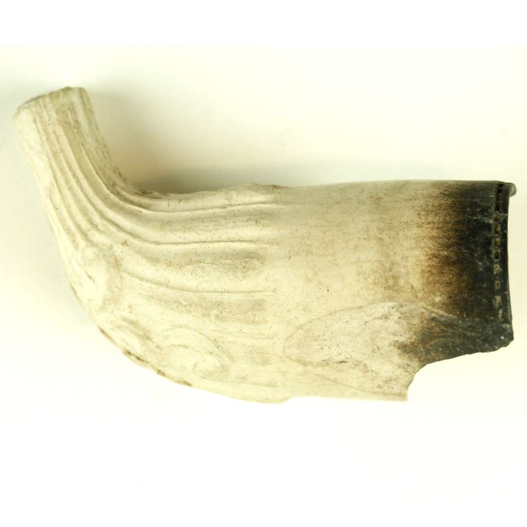 Fragment af kridtpibehoved med del af stilk. Hovedet forneden og stilken riflet. Stemplet oprejst løve (?) med sværd (?) i poterne. Hovedets længde: 4,7 cm.