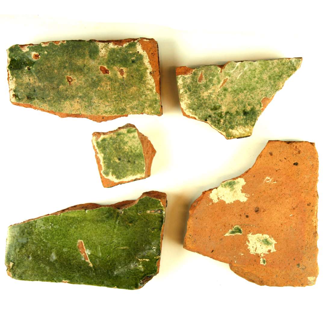 5 fragmenter af gulvfliser af rødbrændt ler. Overfladen begittet og grønt blyglasseret. Nedslidningsgraden forskellig. Opr. formentlig kvadratisk. Bredde: 15,5 cm. Tykkelse: 2,5 - 3 cm.
